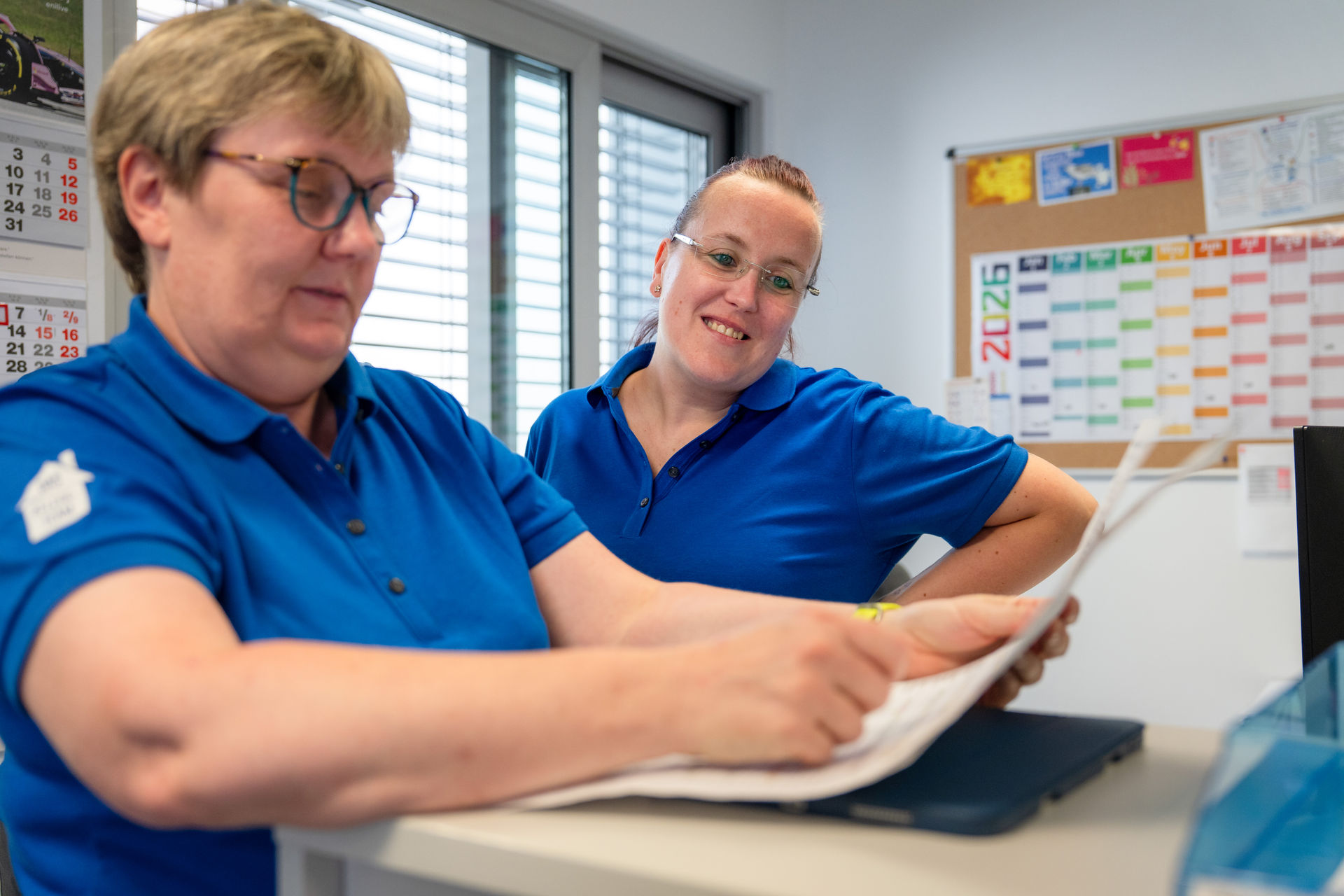 Zwei Mitarbeiterinnen des Pflegeteams stimmen sich anhand von Unterlagen ab