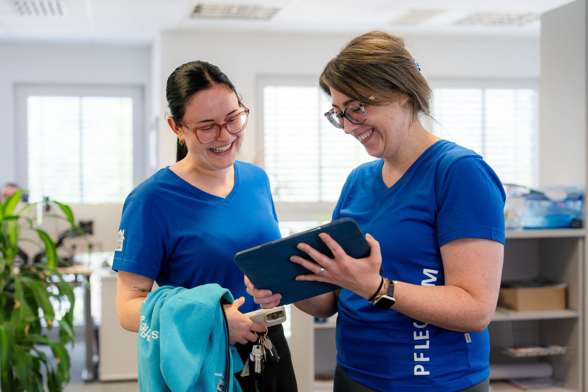 Pflegekräfte des Pflegeteams schauen lachend gemeinsam auf ein Tablet
